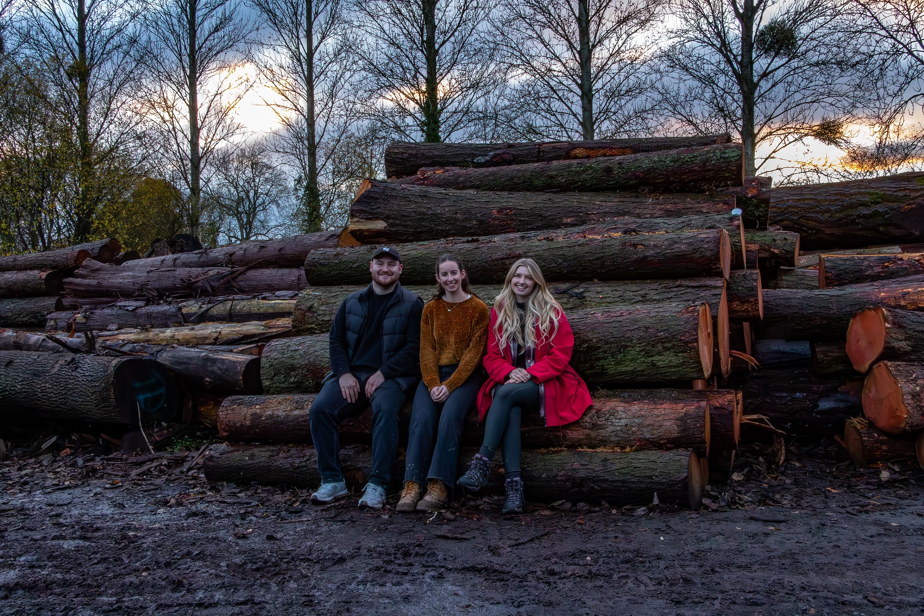 3 students sitting on a large pile of logs